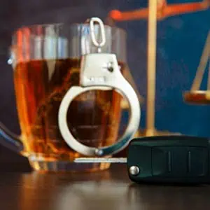 A car key, a glass of alcohol, and hancuffs on a table.
