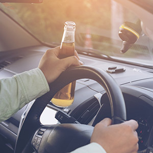  A person's hand on a steering wheel holds a beer bottle, symbolizing a DWI