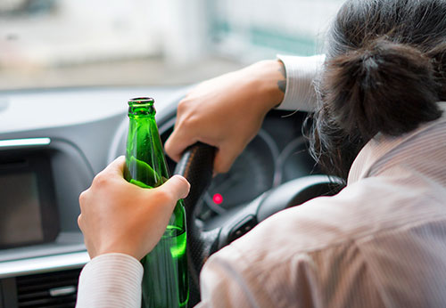 Person drinking an alcoholic beverage while driving, illustrating DWI risk for teachers in New York