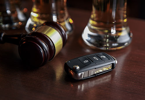 Car keys and a glass of amber-colored alcohol on a dark surface.