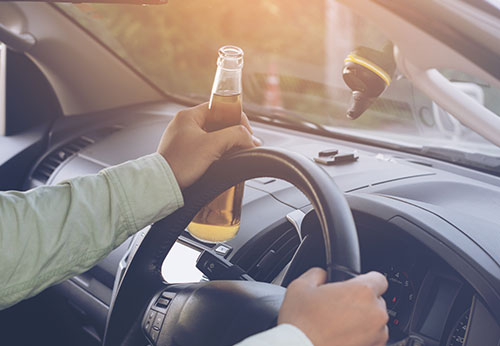 A person driving a car while holding an open beer bottle